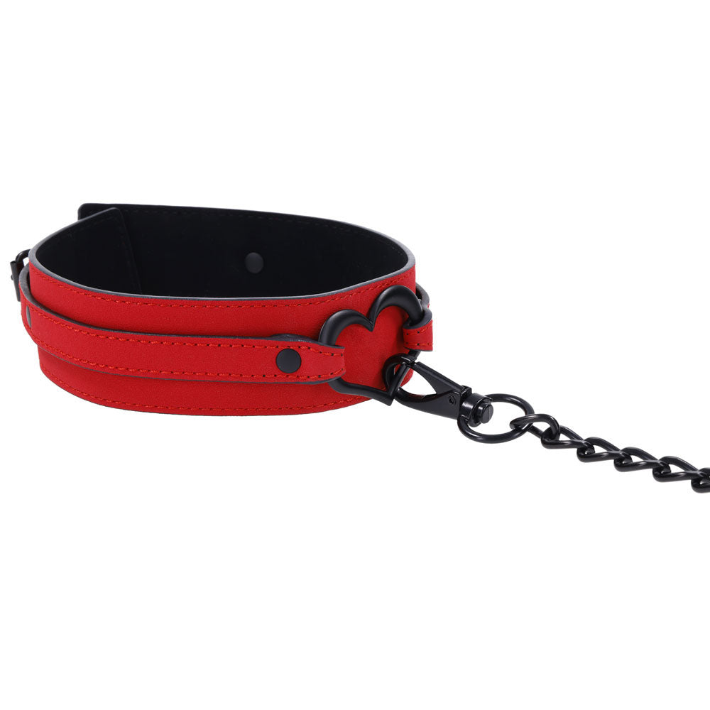 The Sex & Mischief Amor Collar and Leash - Red Restraint features bold red vegan leather with black metal hardware and a heart-shaped loop. It comes with a black chain leash, lined for contrast, making it ideal for those who value style and ethics.