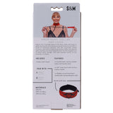 The packaging features a woman with a red vegan leather collar and leash adorned with black heart accents. The Sex & Mischief Amor Collar and Leash - Red Restraint set boasts adjustable vegan leather with a robust buckle, cuffs, and crop. Branding and dimensions are included.