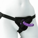 A person wearing the Sex & Mischief Strap-On & Silicone Dildo Kit in black and purple, featuring an adjustable harness around the waist and legs, is shown on a plain white background focusing on the lower torso.