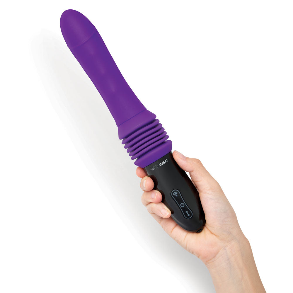 A hand holds the WhipSmart Thrusting Sex Machine, a 23 cm purple vibrator with a smooth, slightly curved shaft and ribbed sections near the base. It has a black handle with two buttons for controlling vibration modes, set against a white background to accentuate its sleek design.