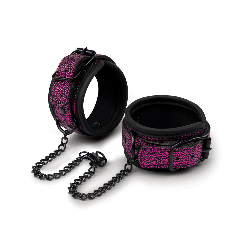 The WhipSmart Dragons Lair Deluxe Wrist & Ankle Cuffs in purple and black are perfect for beginners. They feature a short black chain, adjustable buckles, padded lining, and stylish design with metal rings for easy attachment or detachment.