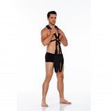 A man stands confidently in a white studio, barefoot in black shorts and the WhipSmart Body Swing - Black Body Swing Harness, adorned with rings and straps. His relaxed stance, with a slight knee bend, speaks volumes. This daring look invites intrigue and adventure as a bedroom essential.