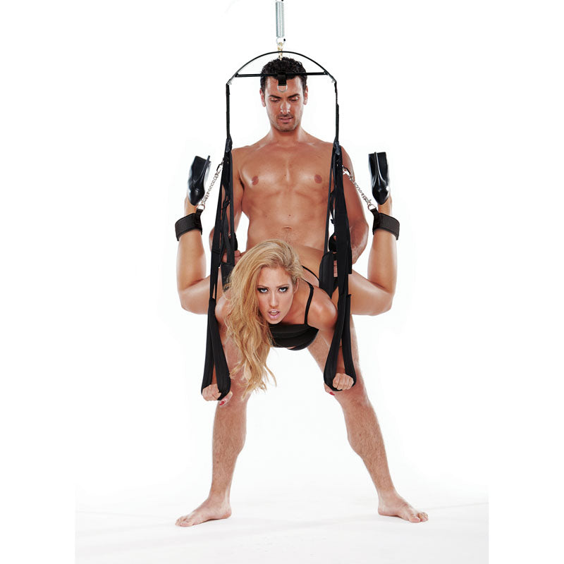 An adventurous couple showcases a daring gymnastic pose using the WhipSmart Fantasy Bondage Swing - Black Swing. The shirtless man, embodying strength, holds her securely mid-air, demonstrating unique balance in this artistic display against a plain white background.