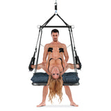 A man sits on a suspended black harness, holding a woman in black lingerie. The WhipSmart Lovebed Lounger Sex Swing adds to their playfulness as the inverted blonde woman gracefully dangles over the cushioned black surface against a white background.