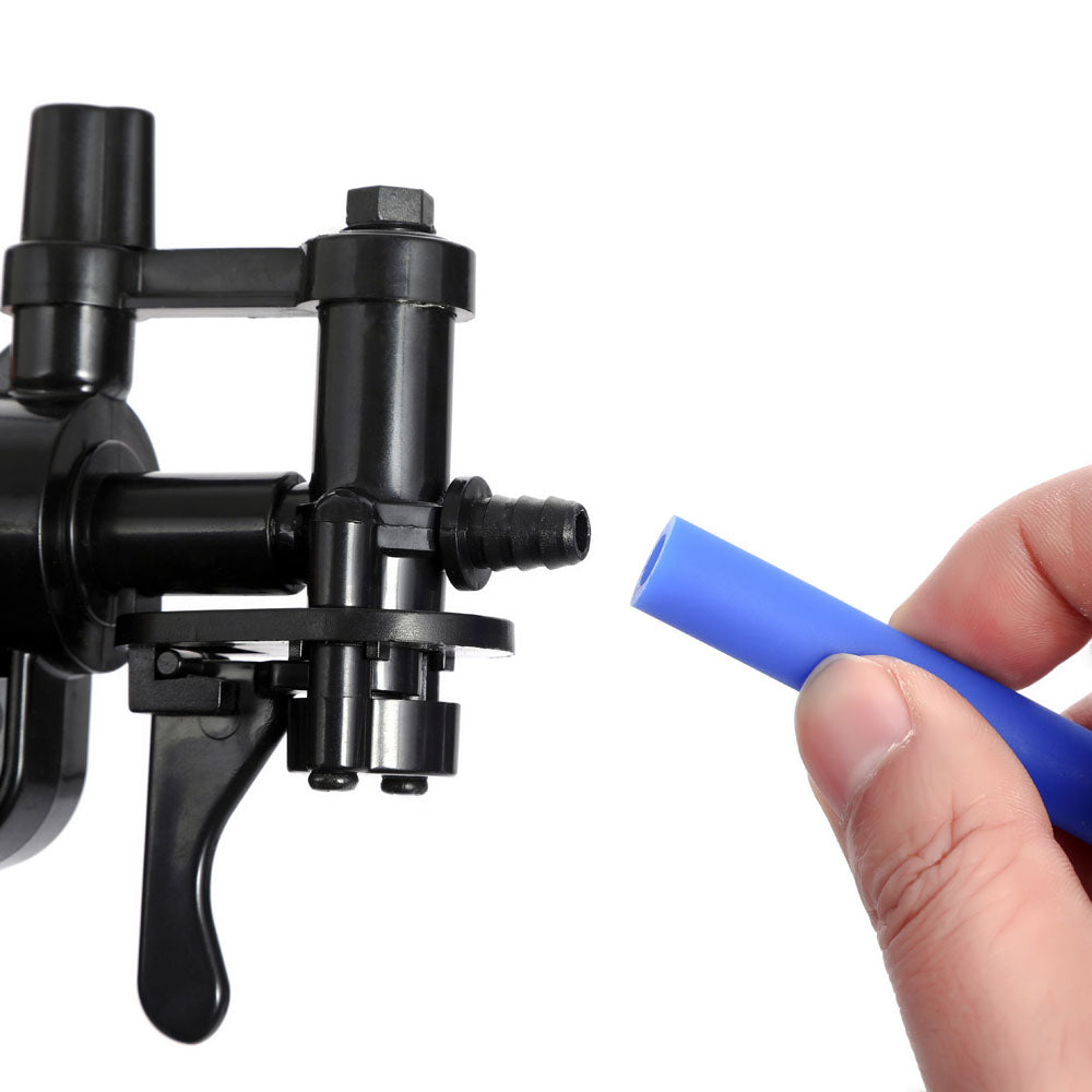 A hand aligns a piece of blue tubing with the black fitting of a LuvPump ProXtra, a clear penis pump featuring a professional gauge. The fittings resemble an enhancement tool with multiple connection points against an uncluttered white backdrop.