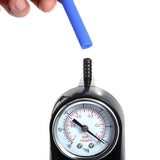 A hand holds the LuvPump ClassiXtra Advanced Power Pump over a black analog pressure gauge. The clear penis pump displays measurements in bar and kPa, with the needle at zero, featuring a black ribbed nozzle for tube attachment against a white background.