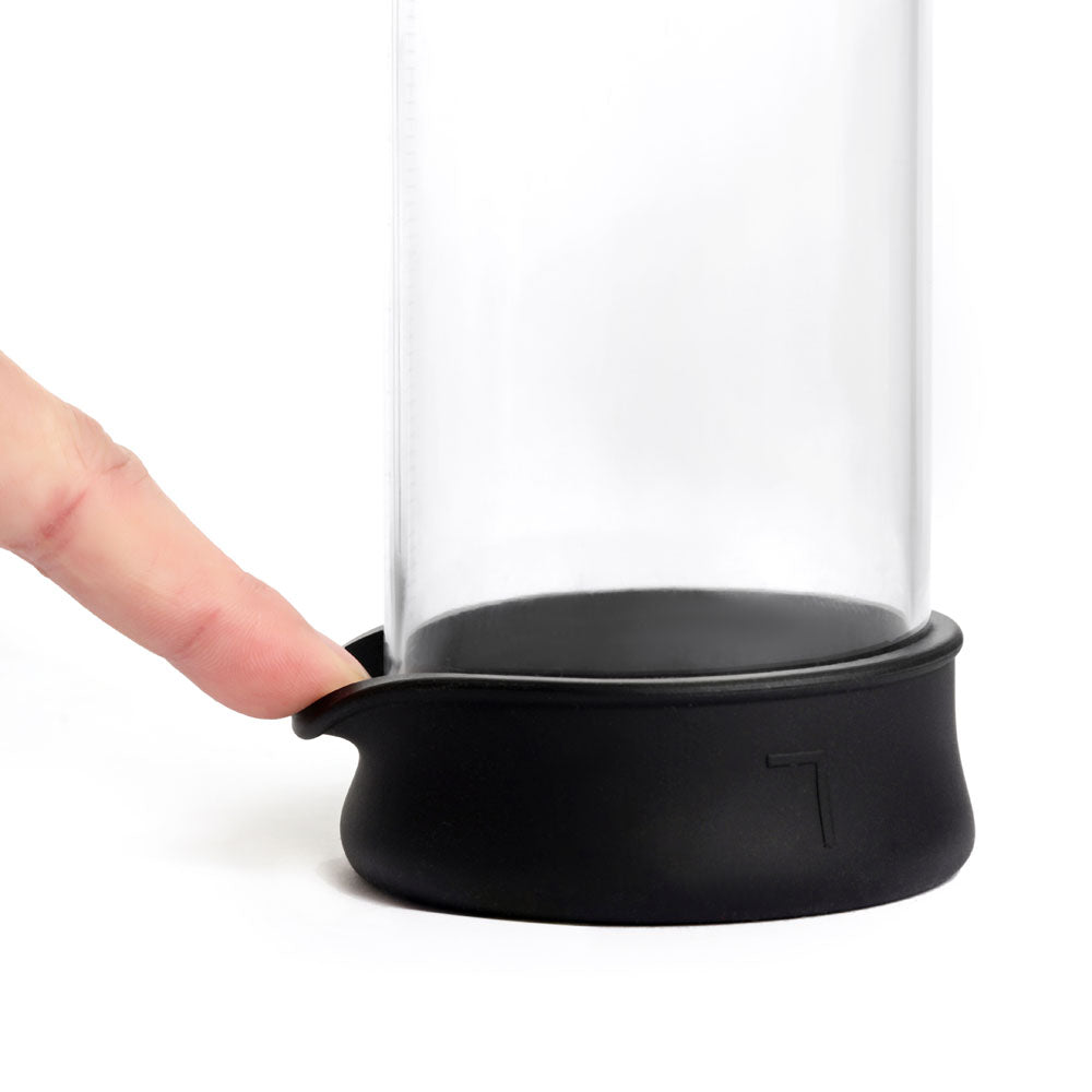 The LuvPump ClassiXtra Advanced Power Pump is a sleek, clear cylindrical container with a black base and engraved logo. A finger presses its side to reveal its subtle design against a white background, combining male sensitivity with curiosity and allure.