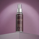 A clear spray bottle with a silver cap, labeled Zero Tolerance Enhancements - The Extra Mile, sits on a glass surface against a muted purple background. The brown label with white text promotes delay spray for men, offering extended performance and stamina in activities.