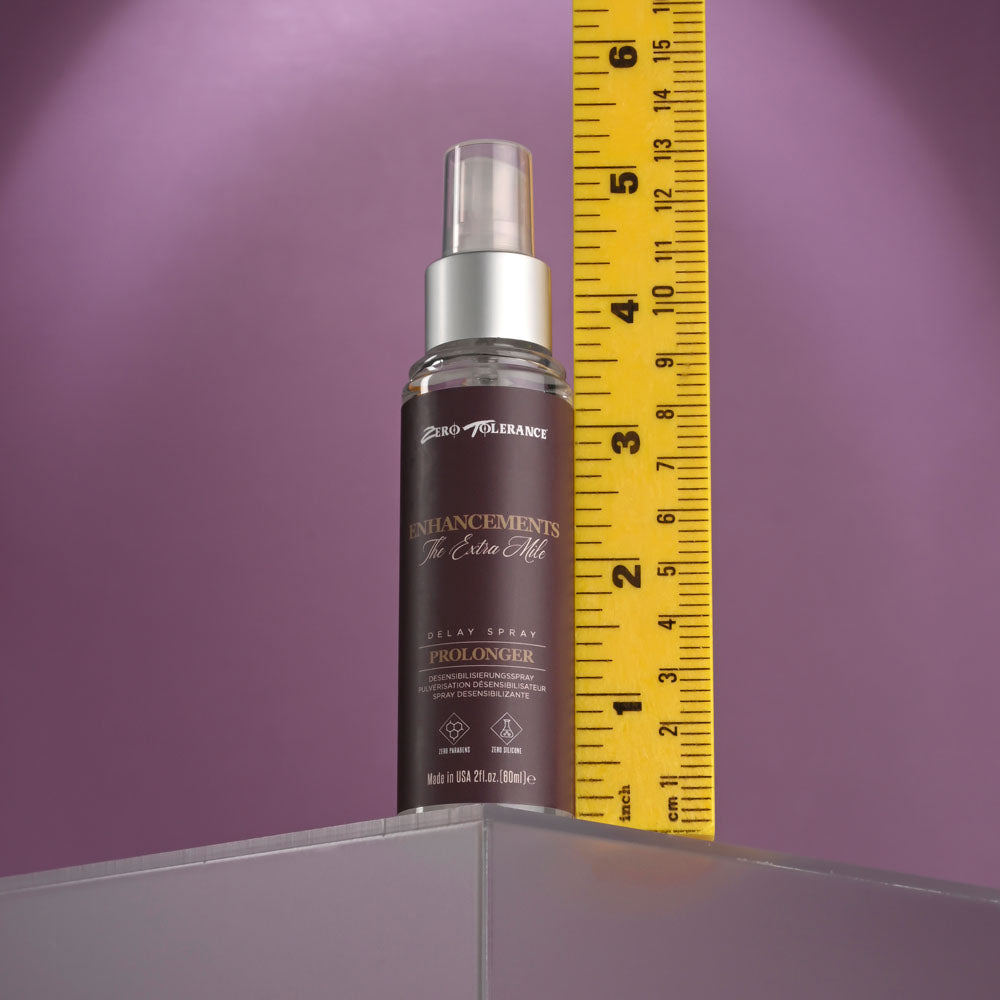 On a purple background, the gray-capped Zero Tolerance Enhancements - The Extra Mile Delay Spray for Men (60 ml) stands vertically, promising enhanced stamina. A yellow measuring tape beside it highlights its height, while its label is adorned with text and logos.