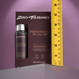 A 60 ml spray bottle of Zero Tolerance Enhancements - The Extra Mile Delay Spray for Men is displayed next to a yellow ruler, indicating its about 5 inches tall. The dark brown packaging with silver text rests on a clear surface against a muted purple background.