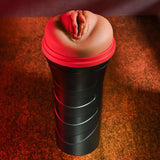 The Zero Tolerance POP ON THE GO Dark - Brown Vagina Masturbator is a black cylindrical stroker with a textured rubber surface and realistic flesh-colored silicone top resembling a travel mug. Warm lighting casts shadows on the textured brown surface underneath.