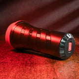 A stylish, metallic red travel mug with a textured grip lies on its side, showcasing subtle pleasure ribs for tactile appeal. It features a black circular base and red lid against a warm reddish-brown backdrop, with lighting enhancing its shiny surface and casting depth-adding shadows.