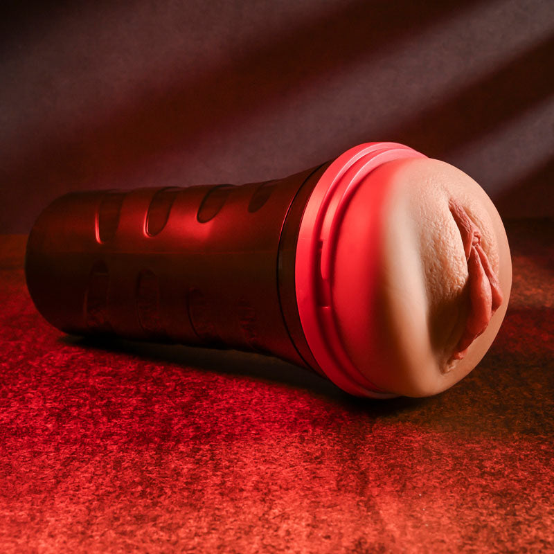 The Zero Tolerance POP ON THE GO Dark - Brown Vagina Masturbator, a cylindrical handheld device resembling a flashlight, features a soft anatomical opening and is highlighted against a textured surface with dramatic red lighting. Its design includes gripping grooves and pleasure ribs for enhanced realism.