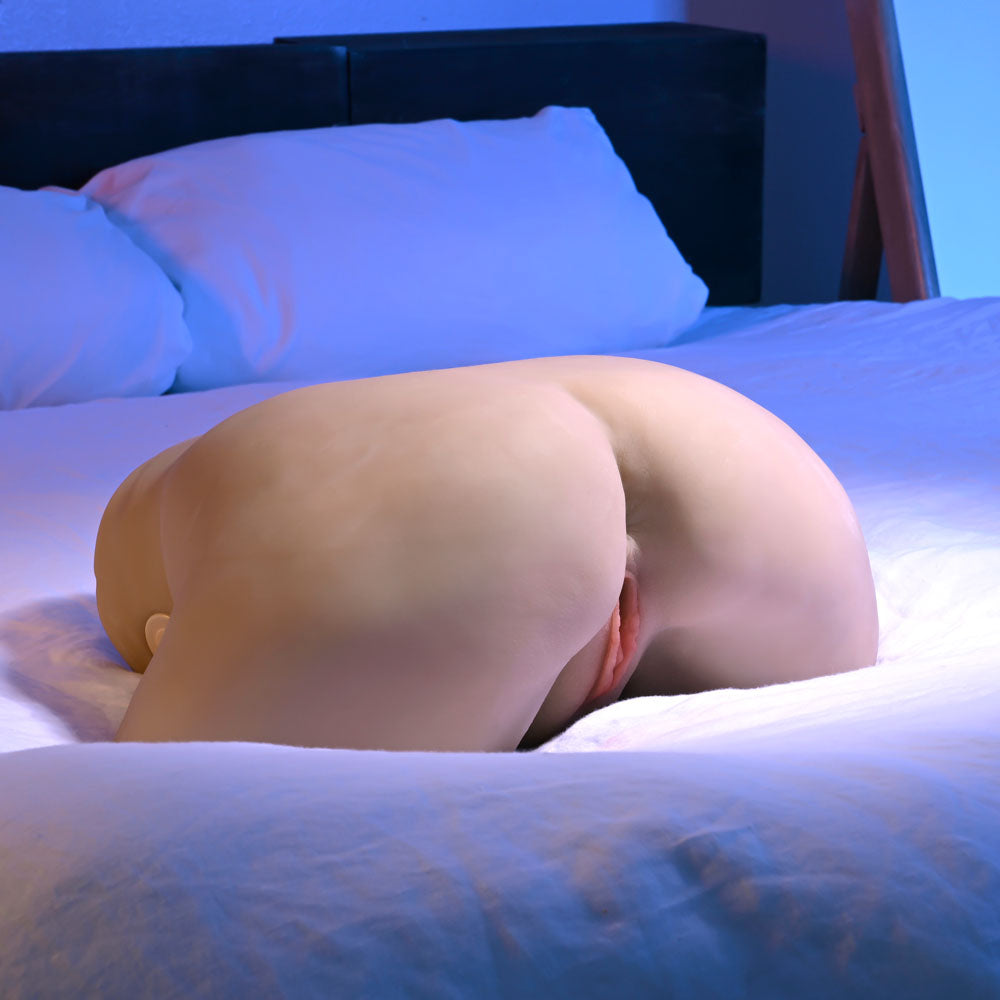 The Zero Tolerance COME PLAY WITH ME - Light - Flesh Lifesize USB Rechargeable Thrusting Torso Masturbator, placed on a bed with white sheets, simulates a life-like stroker experience. The setting includes a dark headboard and pillows, softly illuminated with a bluish tint for an abstract effect.