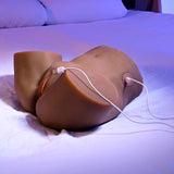 Under blue lighting, a Zero Tolerance COME PLAY WITH ME Dark Brown Lifesize USB Rechargeable Thrusting Torso Masturbator lies on a bed. The model, resembling human anatomy with inserted USB cables, suggests lifelike connectivity amid white pillows enhancing its intriguing realism.