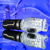 The Zero Tolerance THRILL RIDE, a textured, transparent cylindrical stroker with a black base and metallic accents, rests on a reflective surface against a blue-toned industrial backdrop featuring tubing and machinery. Its waterproof with button-controlled vibrating speeds.