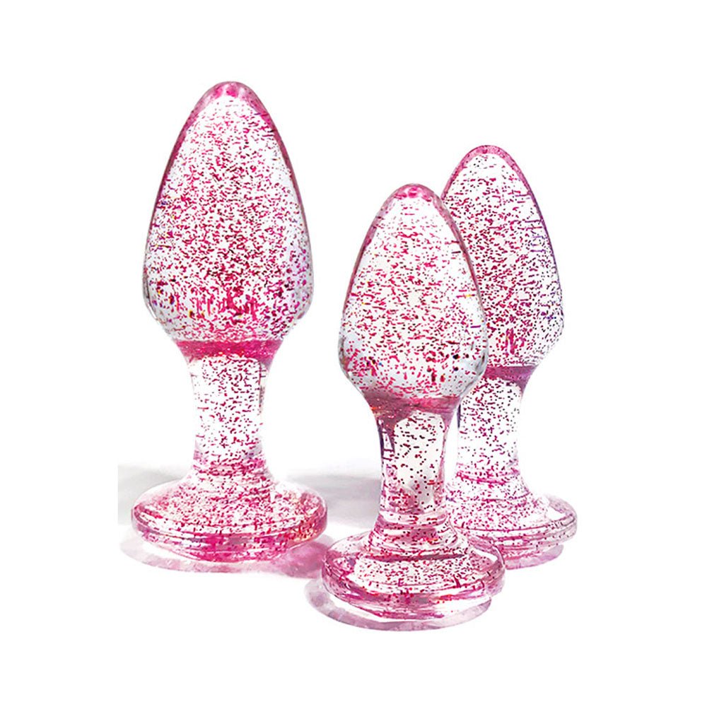 The Adam & Eve Glitter Gem 3-Piece Butt Plug Set displays three upright, pink glittery plugs against a white background. Each has a bulbous top, tapered end, and gem-shaped base for stability, sparkling with pink specks.