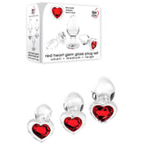 The packaging showcases the Adam & Eve RED HEART GEM GLASS PLUG SET, containing three clear glass butt plugs with red heart-shaped gems, perfect for anal training or temperature play. The brand logo stands out on a pristine white background alongside the elegant plugs.