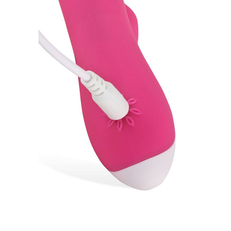 A close-up features a pink USB charging cable inserted into the pink Adam & Eve The Warming Rabbit G Vibrator, with petal-like designs around the port and a white G-Spot tip against a plain white background.