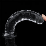 A hand gently touches the Flawless Clear Dildo from the LOVETOY series, revealing its skin-safe transparency and textured, curved glass design. It features a smooth tip and suction cup base, set against a black background to enhance its clarity.