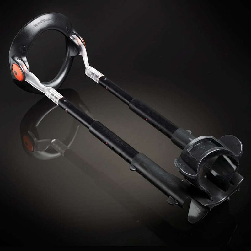 A pair of black ergonomic crutches with curved handles and orange accents sits beside a MaleEdge Pro Kit - Penis Enlarger Kit in Red Case on a reflective dark surface. The crutches feature padded arm supports, adjustable height, clear sections near the handles, and rubberized tips for stability.